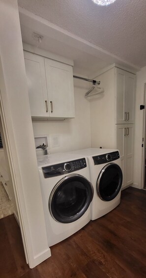 A laundry room with two front-loading washing machines, white cabinets, and a ceiling light. - Cozy 2-bedroom condo in tranquil Kirkland with workspace (Kirkland)