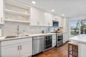A modern kitchen with white cabinetry, stainless steel appliances, and a large window providing a view of the outdoors. - Cozy 2-bedroom condo in tranquil Kirkland with workspace (Kirkland)