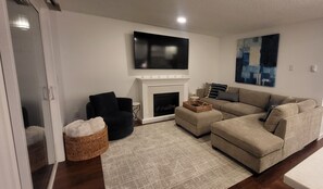 Ein Wohnzimmer mit Kamin, Wandfernseher, Sofa, Sessel und Teppich.
