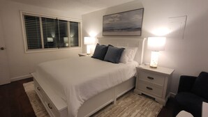 Una camera da letto con un letto, due comodini con lampade, una finestra con persiane, un quadro appeso al muro e una sedia.
