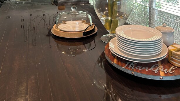 A dining area with a wooden table, clear glass top, and a vase with red flowers.
