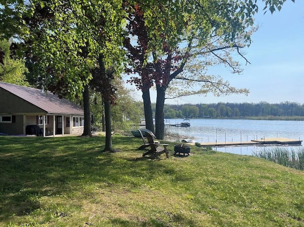 A lakeside property with a covered patio, a grill, and a dock extending into the water.