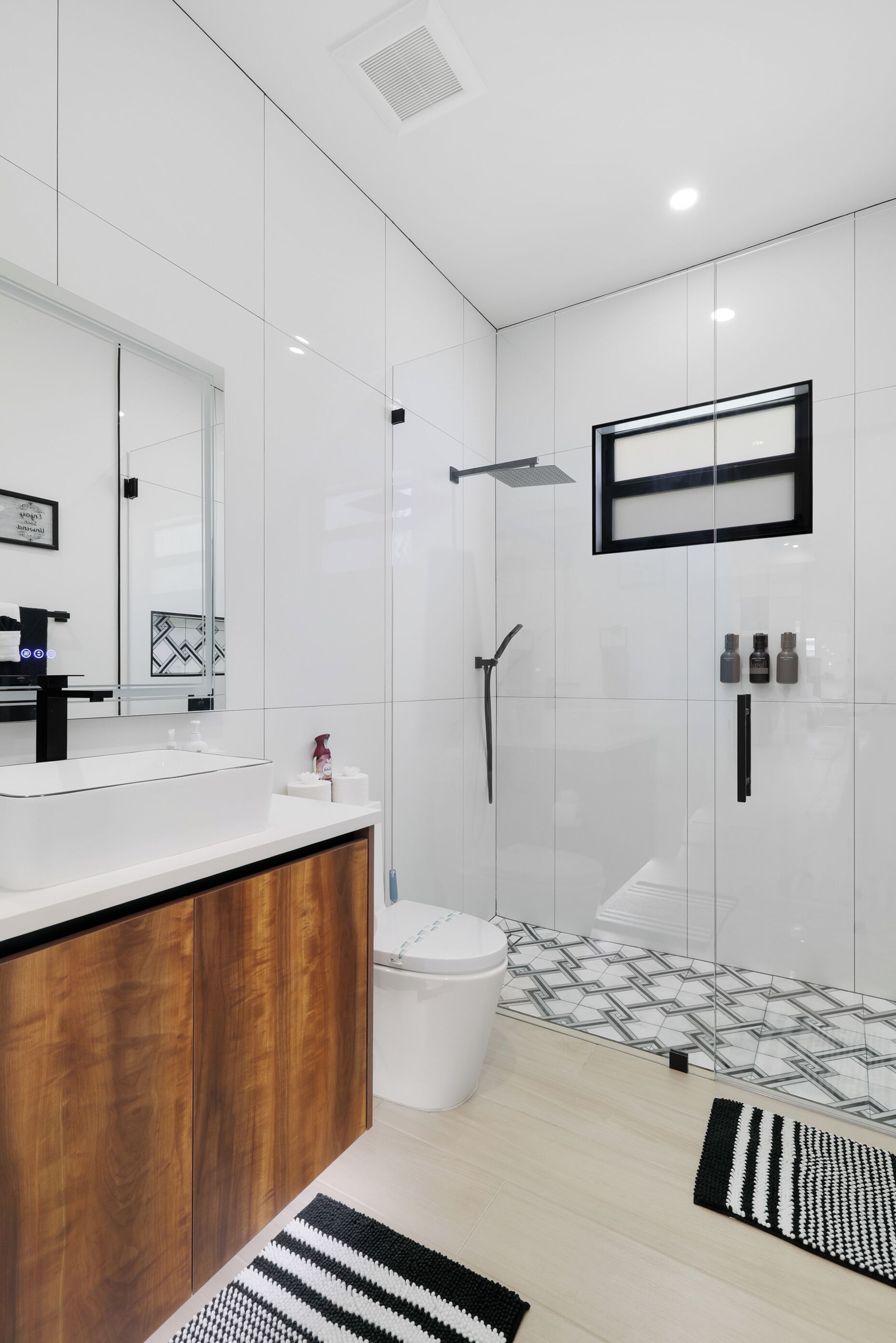 Une salle de bain moderne avec un grand miroir, un meuble-lavabo en bois, une douche et un carrelage décoratif.