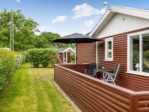 Een houten huis met een terras, een tafel en stoelen.