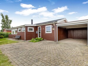 Ett envåningshus i trä med ett garage, en liten uteplats med en bänk och en asfalterad uppfart.