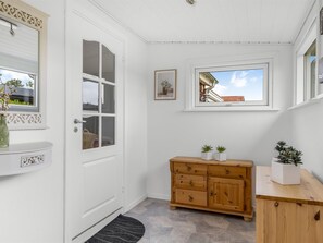 Een witte deur met een ruit, een houten kast met lades, een klein raam met uitzicht en een lijst met een afbeelding aan de muur.