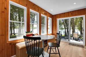 A room with large windows, a wooden interior, a round table, and a bench.