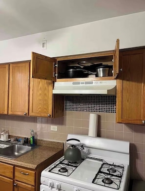 Een keuken met houten kastjes, een fornuis, een spoelbak en een betegelde achterwand.