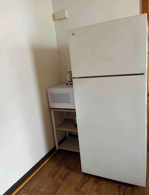 Pieni keittokomero, jossa on valkoinen jääkaappi, mikroaaltouuni ja kahvinkeitin, ja kaikki sijoitettu puiseen työtasoon.