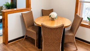 Un comedor con una mesa redonda de madera, cuatro sillas de mimbre, un florero con flores y un espejo en la pared.