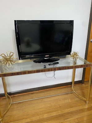 Een televisie op een glazen en metalen tv-meubel met een houten onderstel.
