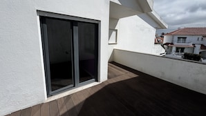 Un edificio moderno con un amplio ventanal corredera, una terraza de madera y una pared exterior blanca.