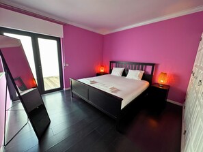 A bedroom with a bed, two bedside lamps, a nightstand, a mirror, and a sliding door leading to a balcony. - Cascais House - Pool (Parede)