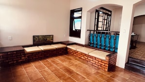 A spacious room with a brick bench, a blue cushioned seating area, and a staircase leading to an upper level. - Zyra's House in Villas - 12 min from the Airport (Lauro de Freitas)