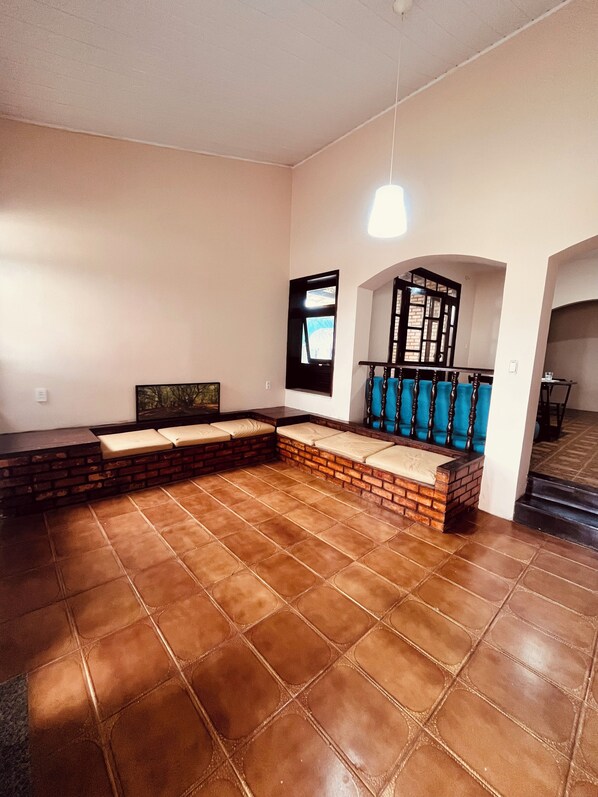 A spacious room with a brick bench, a blue cushioned seating area, and a staircase leading to an upper level.