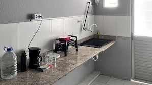 A compact kitchen with a granite countertop, a built-in sink, a ceiling fan, and a window providing natural light. - Zyra's House in Villas - 12 min from the Airport (Lauro de Freitas)