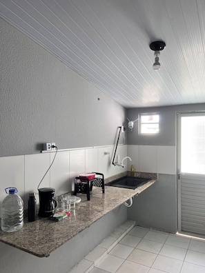 Uma cozinha compacta com bancada de granito, pia embutida, ventoinha no teto e janela que ilumina naturalmente.