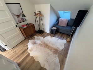 Ein Zimmer mit Holzboden, einem Kuhfellteppich, einer Couch mit rosa Kissen, einem Holzkasten und einem gerahmten Bild an der Wand.