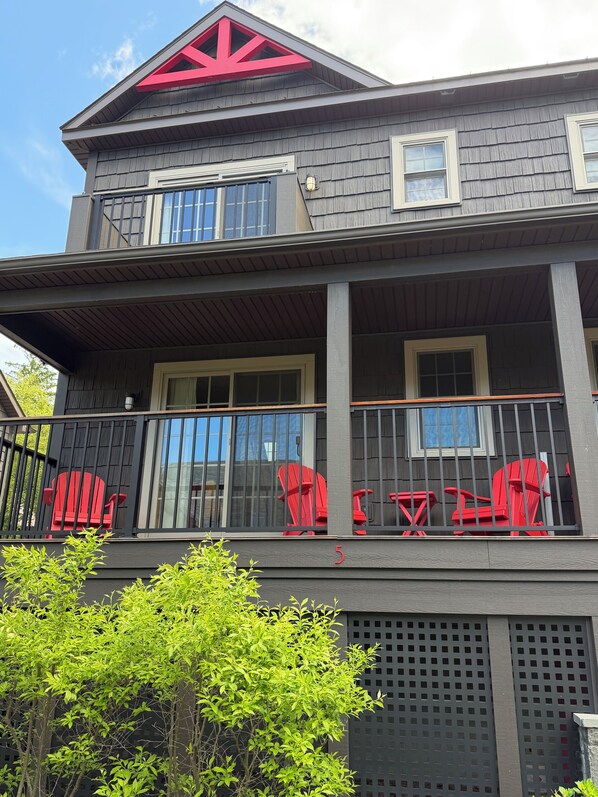 Un edificio de dos pisos con un balcón, sillas Adirondack rojas y un logotipo rojo grande en el techo.