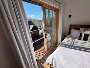 Un dormitorio con cama, ventana con cortinas y vista a una casa y árboles.
