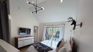 Quarto com cama, televisão, penteadeira, candelabro e vista para o exterior.