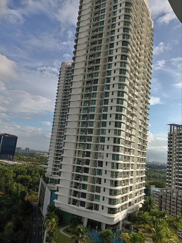 A high-rise building with multiple balconies, surrounded by greenery and other buildings.