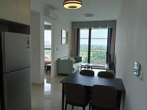 Uma cozinha compacta com geladeira, uma mesa de jantar com cadeiras, um sofá e uma janela grande com cortinas.