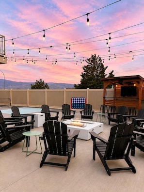 An outdoor seating area with chairs and a fire pit, a pool, and a TV screen.