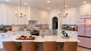 Une cuisine moderne avec des meubles blancs, un îlot central doté de tabourets de bar et un réfrigérateur en acier inoxydable.