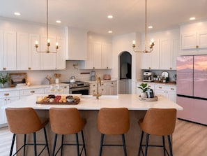 Una cocina moderna con armarios blancos, una isla central con taburetes de bar y un refrigerador de acero inoxidable.