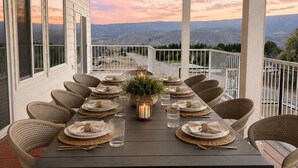 Un espace extérieur abrité, aménagé pour les repas, avec une table dressée pour six personnes, entouré de chaises en osier et offrant une vue panoramique.