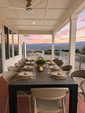 Un espacio comedor al aire libre cubierto con una mesa dispuesta para seis personas, rodeado de sillas de mimbre y vistas panorámicas.