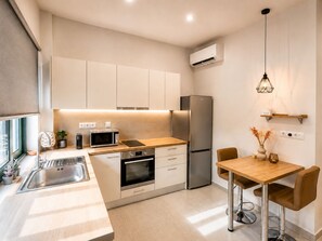 Eine moderne Küche mit Einbauofen, Mikrowelle und Edelstahlkühlschrank. Ein Holztisch mit Stühlen und eine Pendelleuchte sind ebenfalls vorhanden.