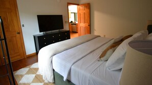 Un dormitorio con una cama, un televisor sobre un tocador y una cocina al fondo.