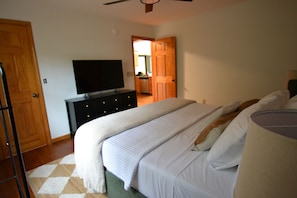 Une chambre avec un lit, un téléviseur posé sur une commode, et une cuisine à l’arrière-plan.