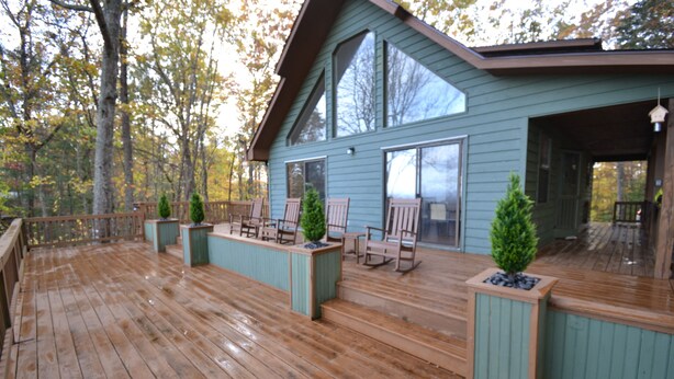 Una terraza de madera con zona de estar cubierta, ventanas amplias y vistas al bosque circundante.