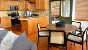 Una cocina con armarios de madera, una zona de comedor con una mesa redonda y sillas, y una escalera que sube a un nivel superior.