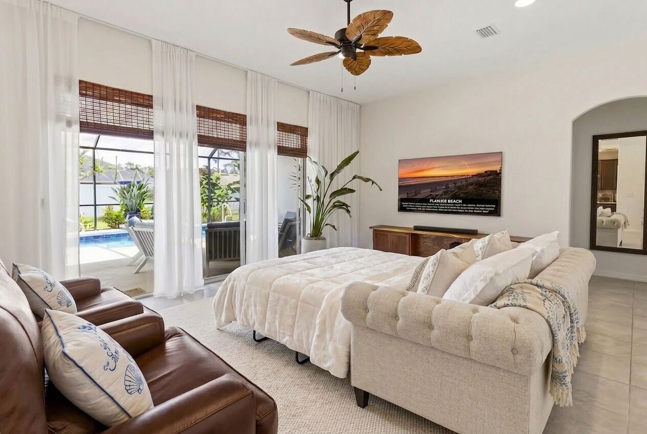 Un dormitorio con cama, sofá, ventilador de techo, televisor y vistas al exterior.