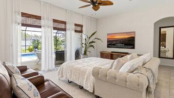 Un dormitorio con cama, sofá, ventilador de techo, televisor y vistas al exterior.