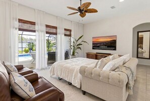Une chambre avec un lit, un canapé, un ventilateur de plafond, une télévision et une vue sur l’extérieur.