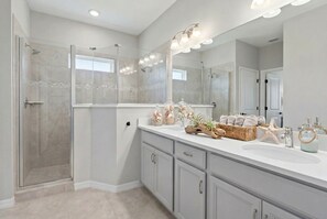 Un baño moderno con cabina de ducha de vidrio, un espejo grande y un tocador con una cesta de toallas.