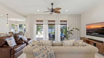 A living room with a brown leather sofa, beige sofa, ceiling fan, large windows, and a painting of Flagler Beach.