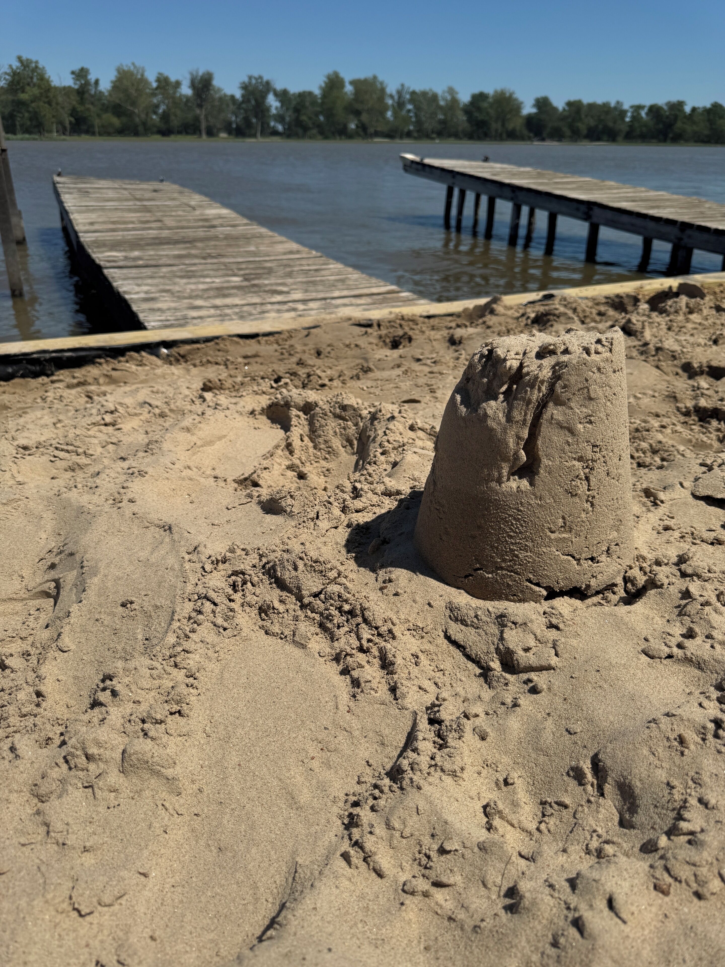 Une plage de sable avec des empreintes, une structure en bois et un ciel dégagé.
