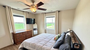 A bedroom with a bed, dresser, ceiling fan, TV, and windows. - Lake Life Starts Here—w/ Dock, Kayaks & Relaxation (Craig)