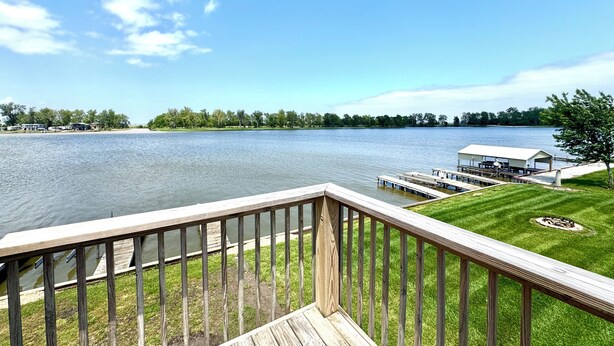 A deck with a view of a lake, dock, and a building across the water. - Lake Life Starts Here—w/ Dock, Kayaks & Relaxation (Craig)