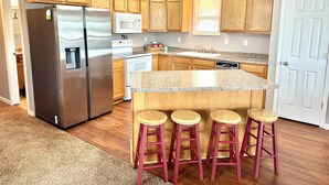 A modern kitchen with wooden cabinets, stainless steel appliances, a granite countertop, and a central island with stools. - Lake Life Starts Here—w/ Dock, Kayaks & Relaxation (Craig)