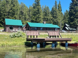Eine Hütte mit grüner Dachbegrünung, einer Holzterrasse und einem Steg, der ins Wasser führt.