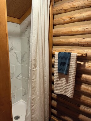 A bathroom with a shower, marble tiles, wooden wall paneling, and a towel rack with a towel. - Harvey’s River Retreat 30 minutes from Yellowstone (Island Park)