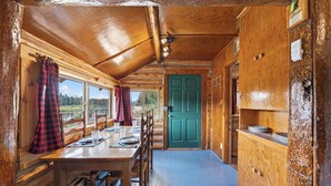 A cabin interior with a dining area, a green door, and a view of the outdoors. - Harvey’s River Retreat 30 minutes from Yellowstone (Island Park)