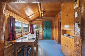 A cabin interior with a dining area, a green door, and a view of the outdoors. - Harvey’s River Retreat 30 minutes from Yellowstone (Island Park)